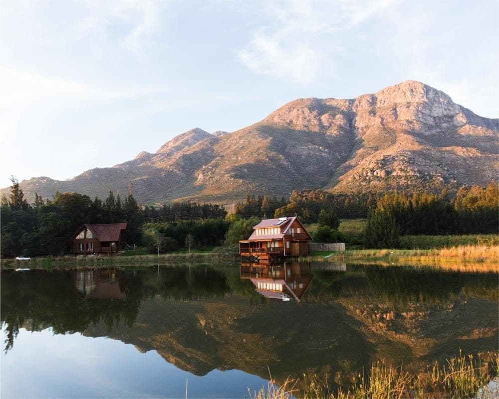 A timber cabin reflected in a farm dam below the mountains